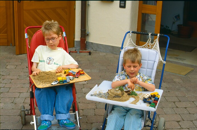 Zwei Jungen sitzen in Kinderwägen und haben vor sich ein Tablett mit Sand und Autos. Sie spielen.