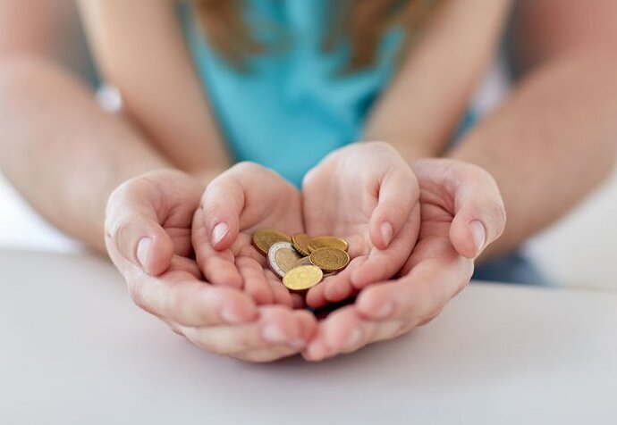 In den Händen einer erwachsenen Person liegen die Hände eines Kindes. In den Händen des Kindes liegen Euromünzen.