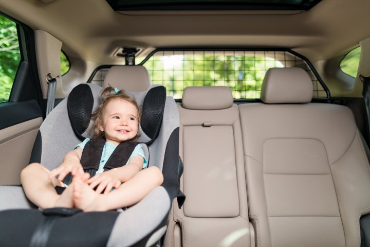 Ein kleines Mädchen sitzt in ihrem Kindersitz auf der Rückbank eines Autos. Es lacht und schaut aus dem Fenster.