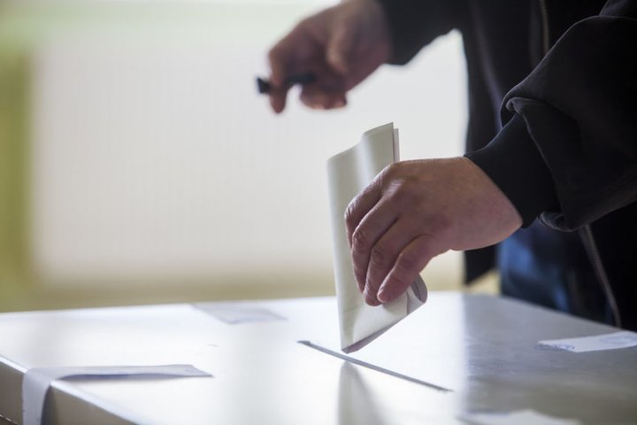 Nahaufnahme: Eine Person wirft einen Wahlzettel in eine Wahlurne.
